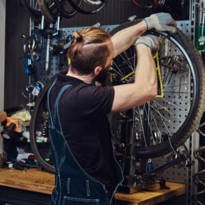 handsome redhead male jeans coverall working with bicycle wheel repair shop worker removes bicycle tire workshop